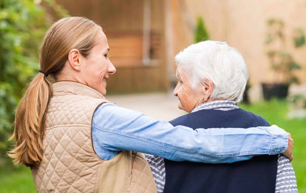 Senior assisted living patient walking outdoors with her daughter on a paved path at Traditions at North Willow
