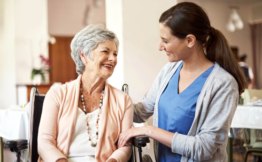 Senior memory care resident at Traditions at North Willow sitting in her wheelchair as her caregiver looks at her
