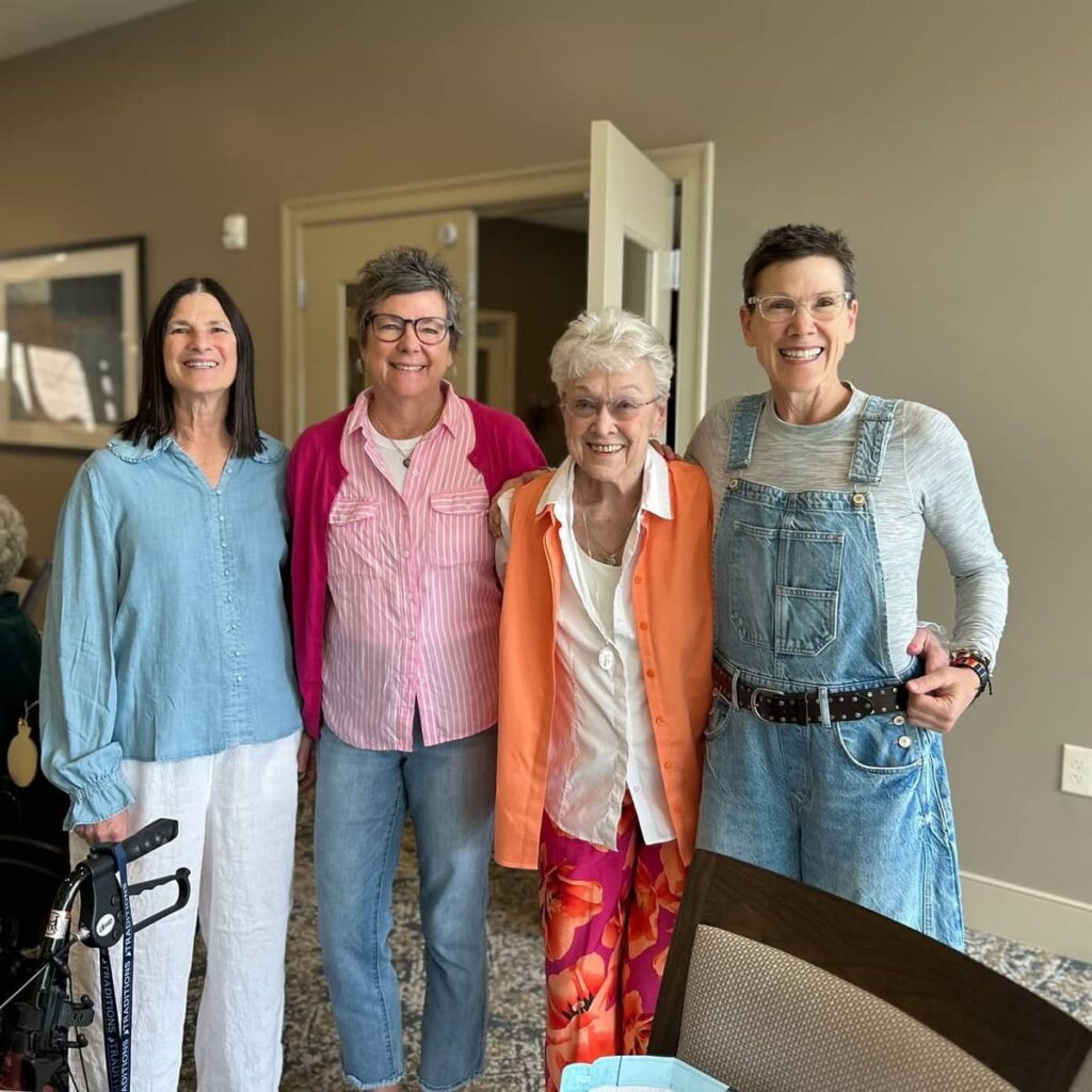 Four women smile together in the hallway at Traditions at North Willow during a visit.