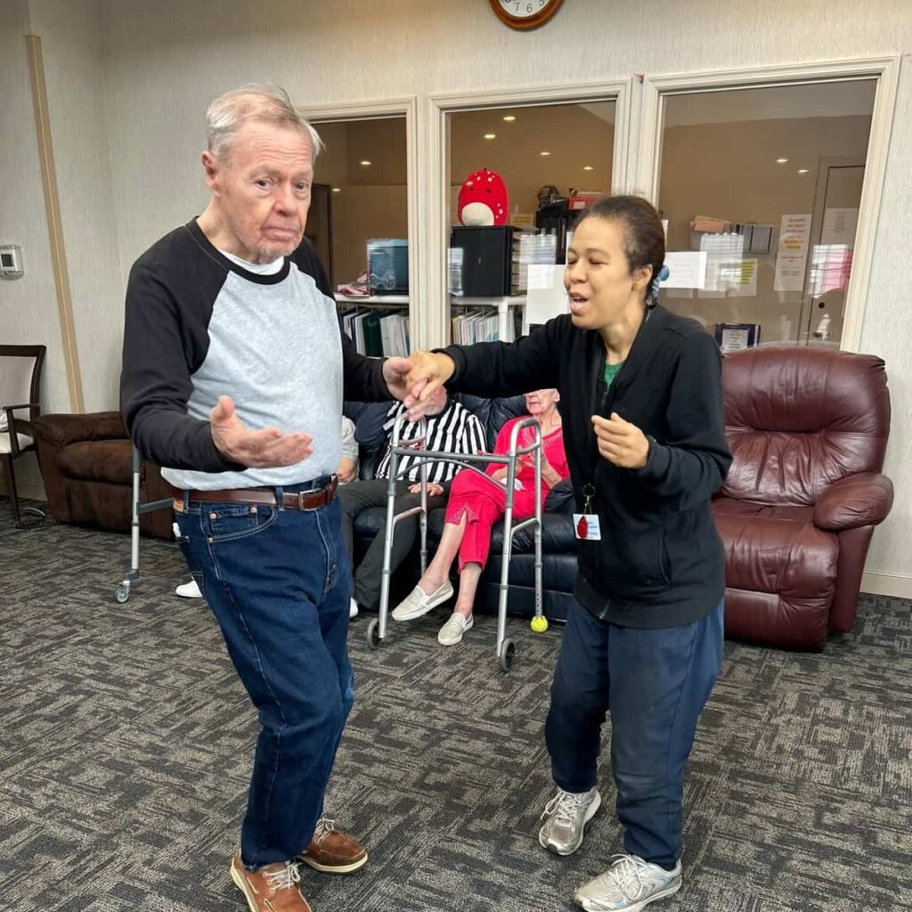 A resident dances with a Traditions at North Willow team member during a social activity in the community common area.