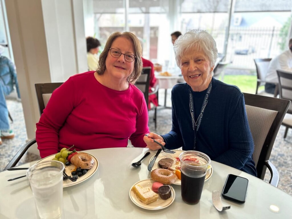 Two residents enjoy breakfast together at Traditions at North Willow, sharing plates of bagels, pastries, and fresh fruit.