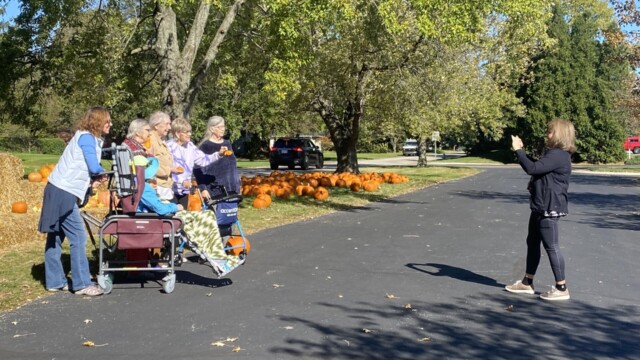 Photo of the Traditions activity director taking a photo of seniors outdoors at a Fall event